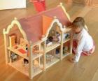 Niña jugando con una muñeca y una casita de muñecas con muebles