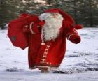 Papá Noel cargando con el gran saco de regalos de Navidad por el bosque