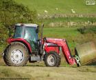 Un tractor rojo transportando una paca de hierba