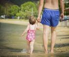 Padre y su hija pequeña paseando por la playa en un día de verano