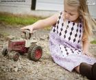 Una niña sentada en el suelo jugando con un tractor rojo