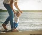 Bebé ayudado por su padre, andando por la orilla del mar